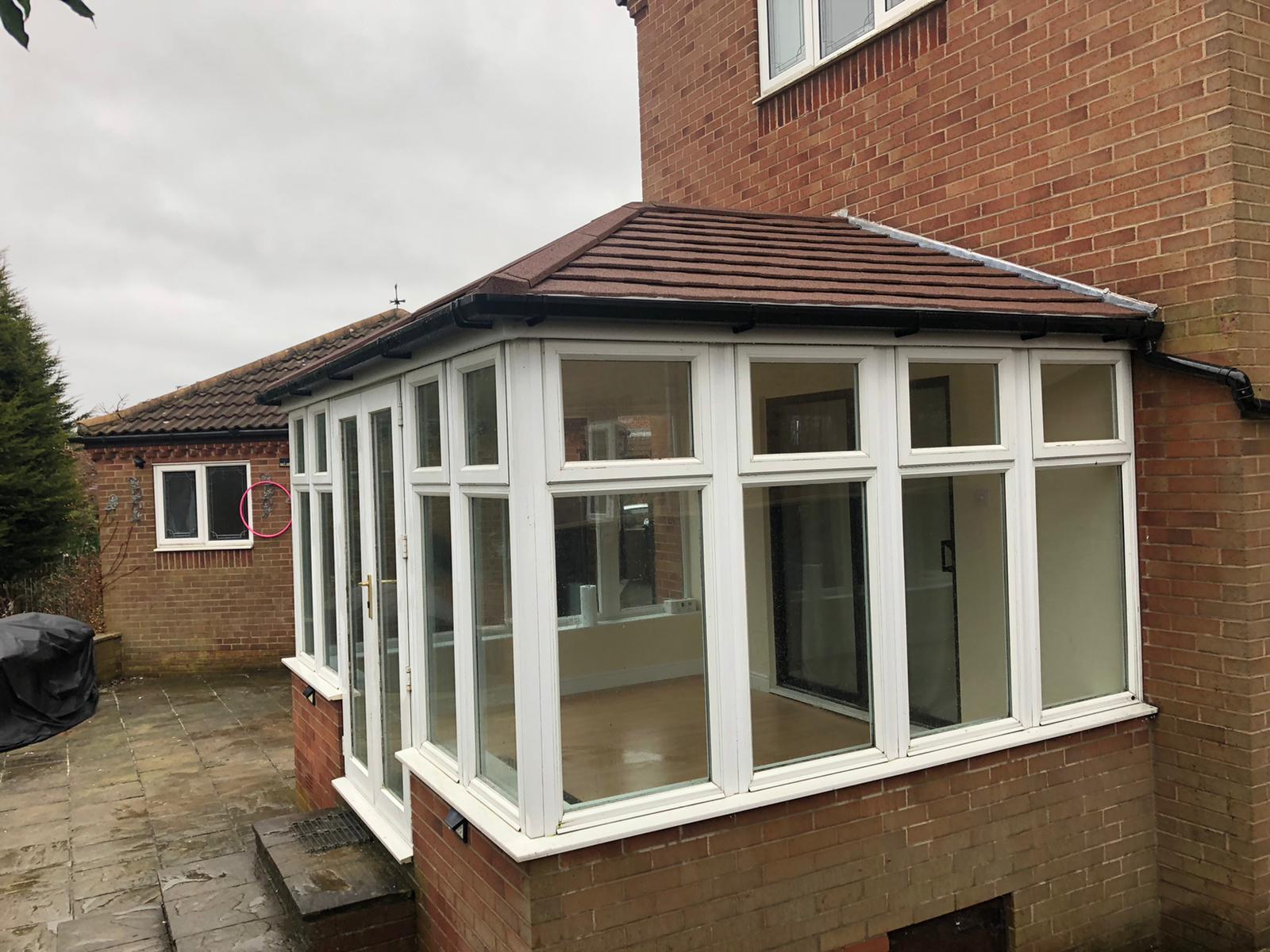 A large brick house with a downstairs conservatory in the foreground. A small concrete patio to the immediate left.